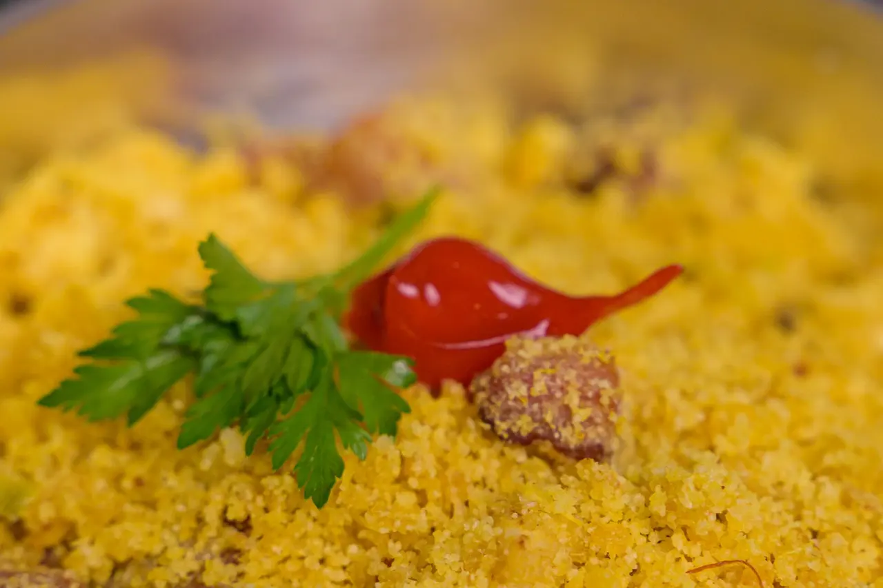 Farofa amarela com pedaços de linguiça numa panela de alumínio, enfeitada com salsinha e uma pimenta vermelha.