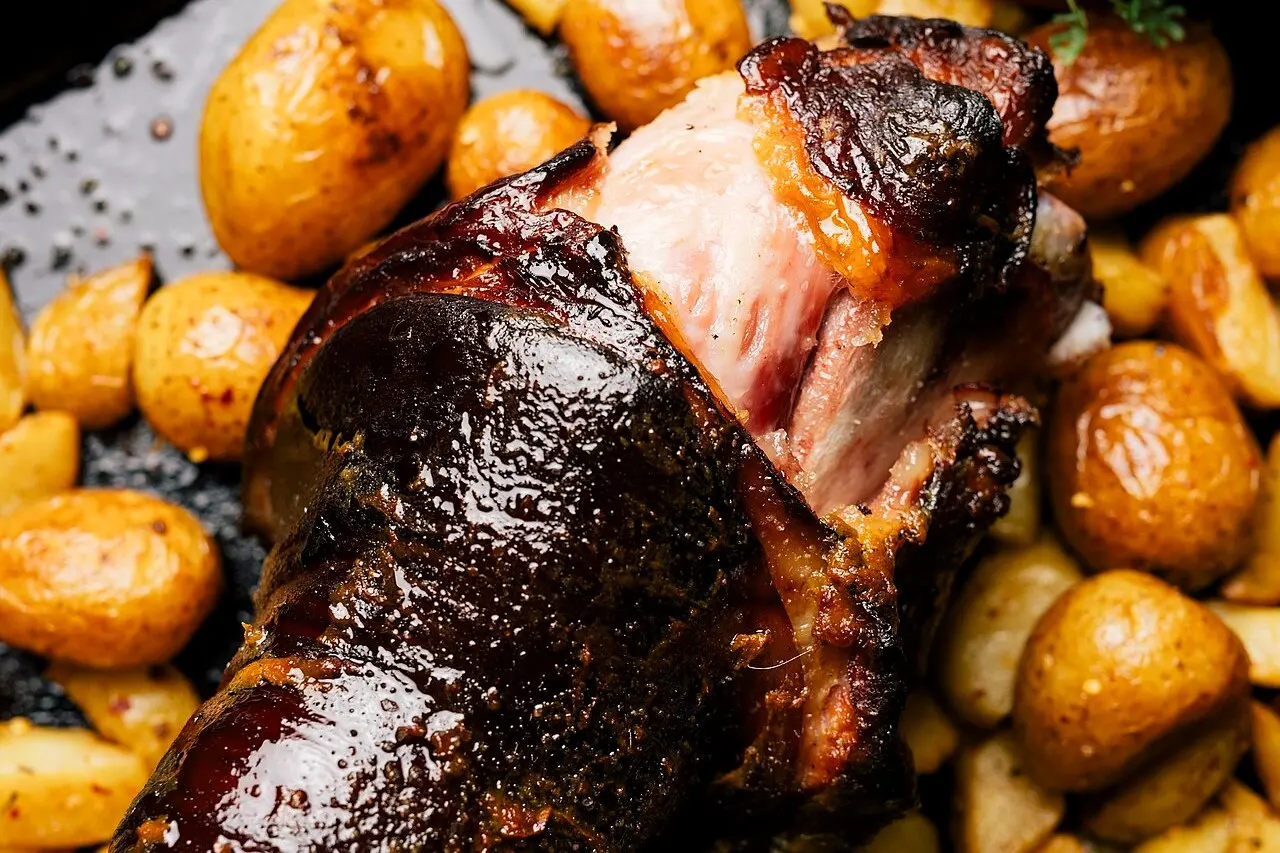 Pernil de porco assado, com a pele escura e brilhante e um corte que mostra a carne, numa assadeira com batatas.